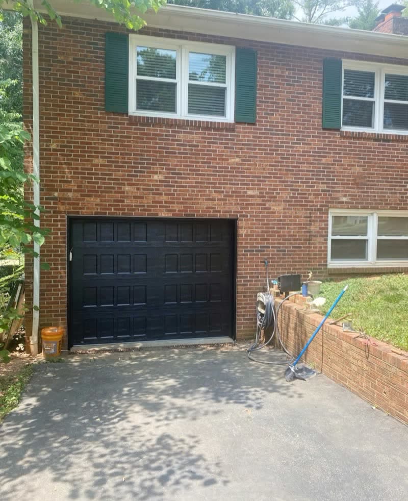 After: new black raised-panel door on the same brick home